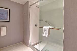 Un baño moderno con cabina de ducha de vidrio, una toalla blanca en un perchero y una obra de arte enmarcada en la pared.