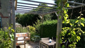 Une terrasse de jardin agrémentée d’une pergola en bois, d’une table et d’un banc.
