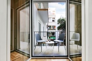 A balcony with two chairs and a table, a bottle of wine, and a view of a building with balconies. - Brand New Modern Apartment (Athens)