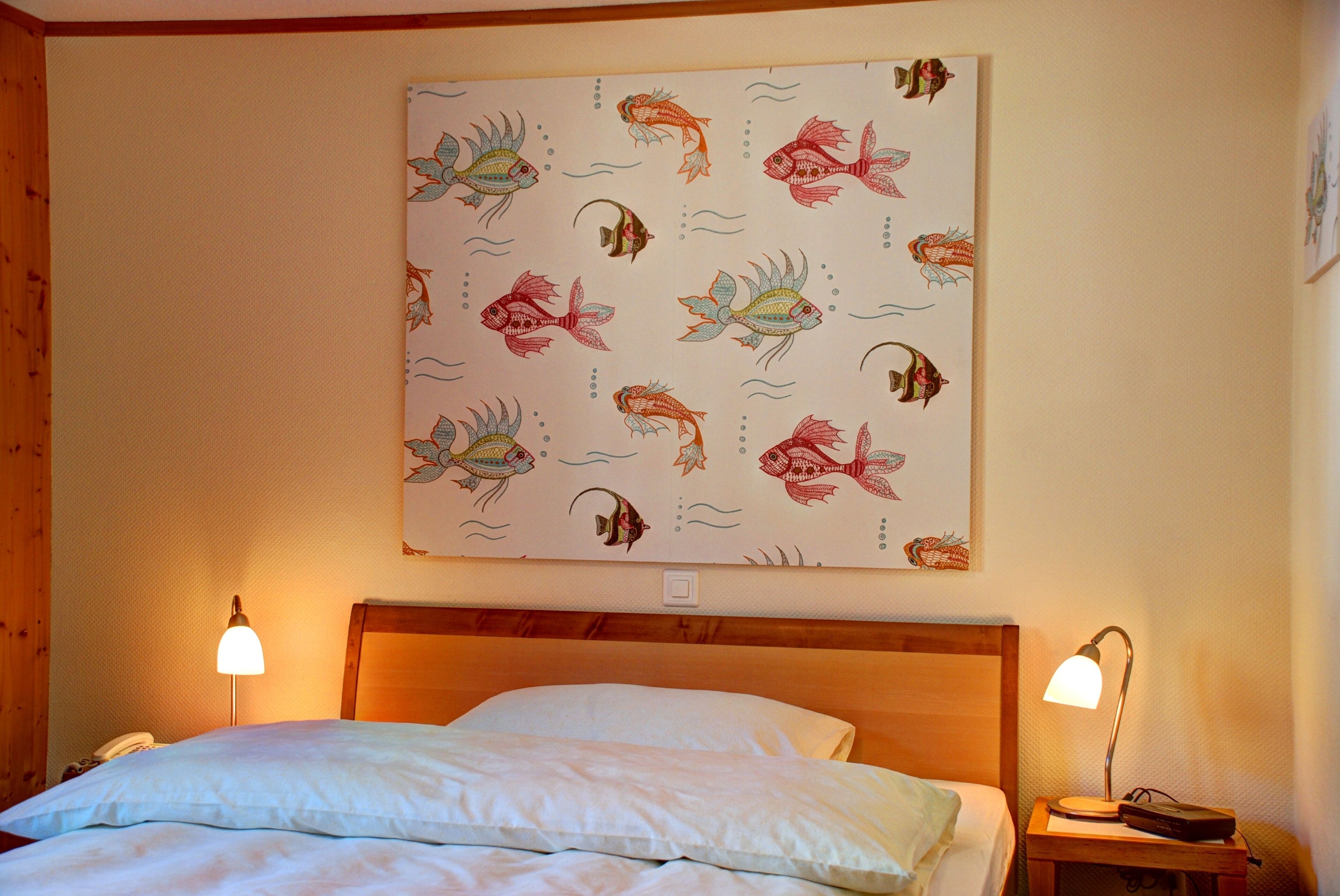 A hotel room with a bed, two bedside lamps, and a wall with a fish pattern.