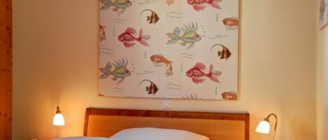 A hotel room with a bed, two bedside lamps, and a wall with a fish pattern.