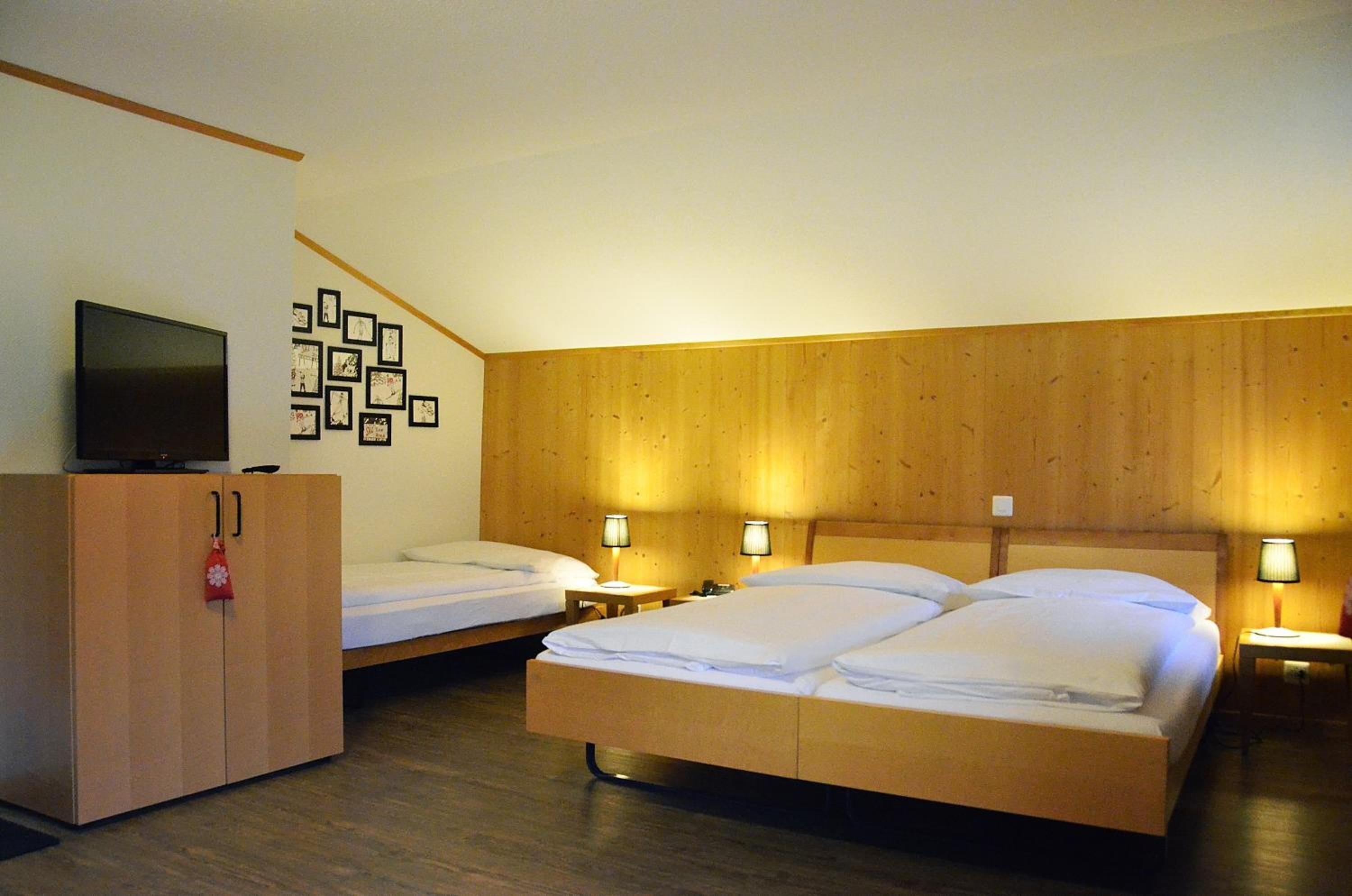 A hotel room with two beds, a TV, wooden paneling, and wall-mounted lamps.