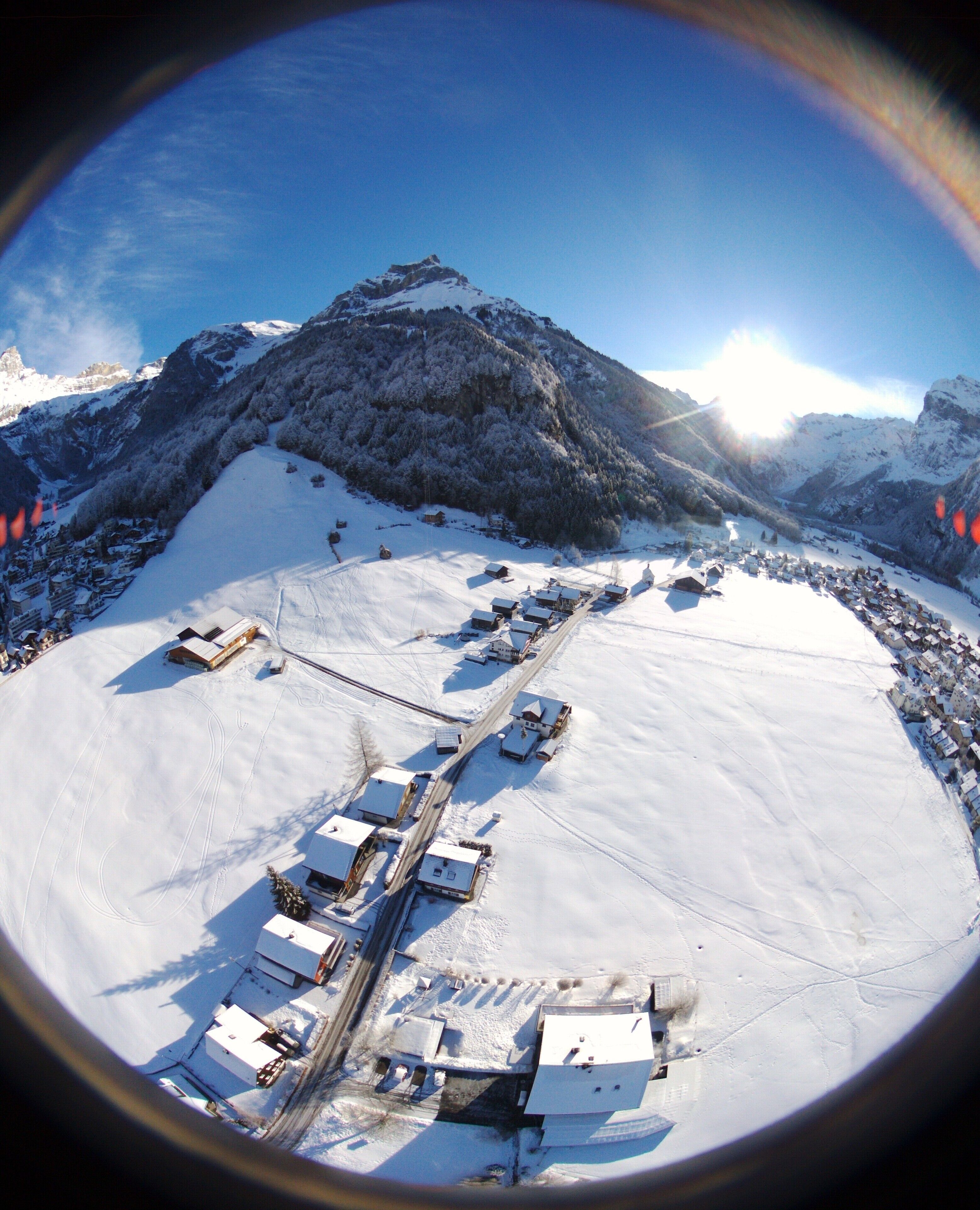 A panoramic view of a snow-covered mountain area with a small settlement, including buildings and a road.