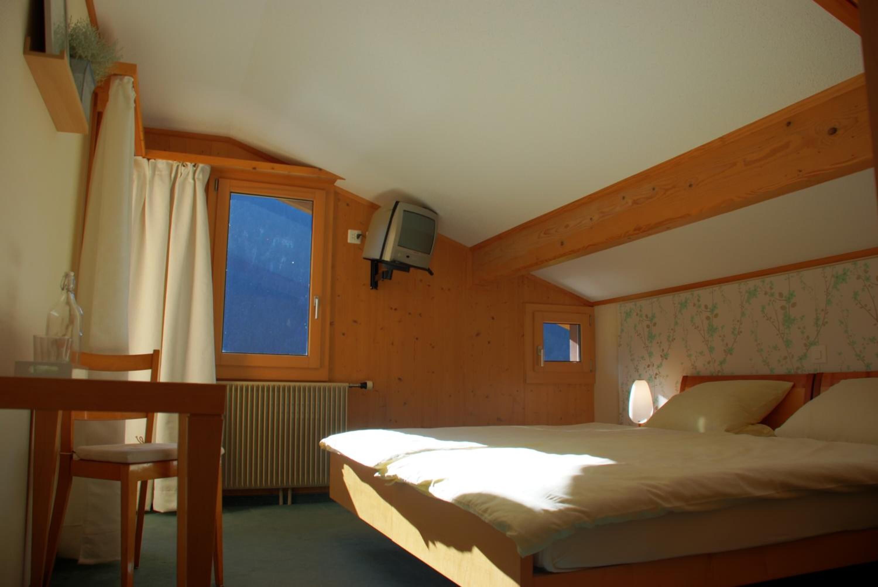 Un dormitorio con techo de madera, una cama, un ventanal pequeño, un televisor y un radiador.