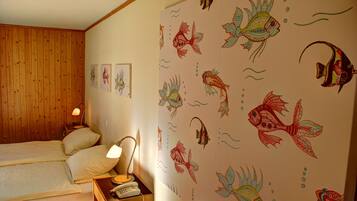 A bedroom with a wooden paneled wall, a bed with two pillows, a bedside table with a lamp and a telephone, and a wall with a fish pattern.