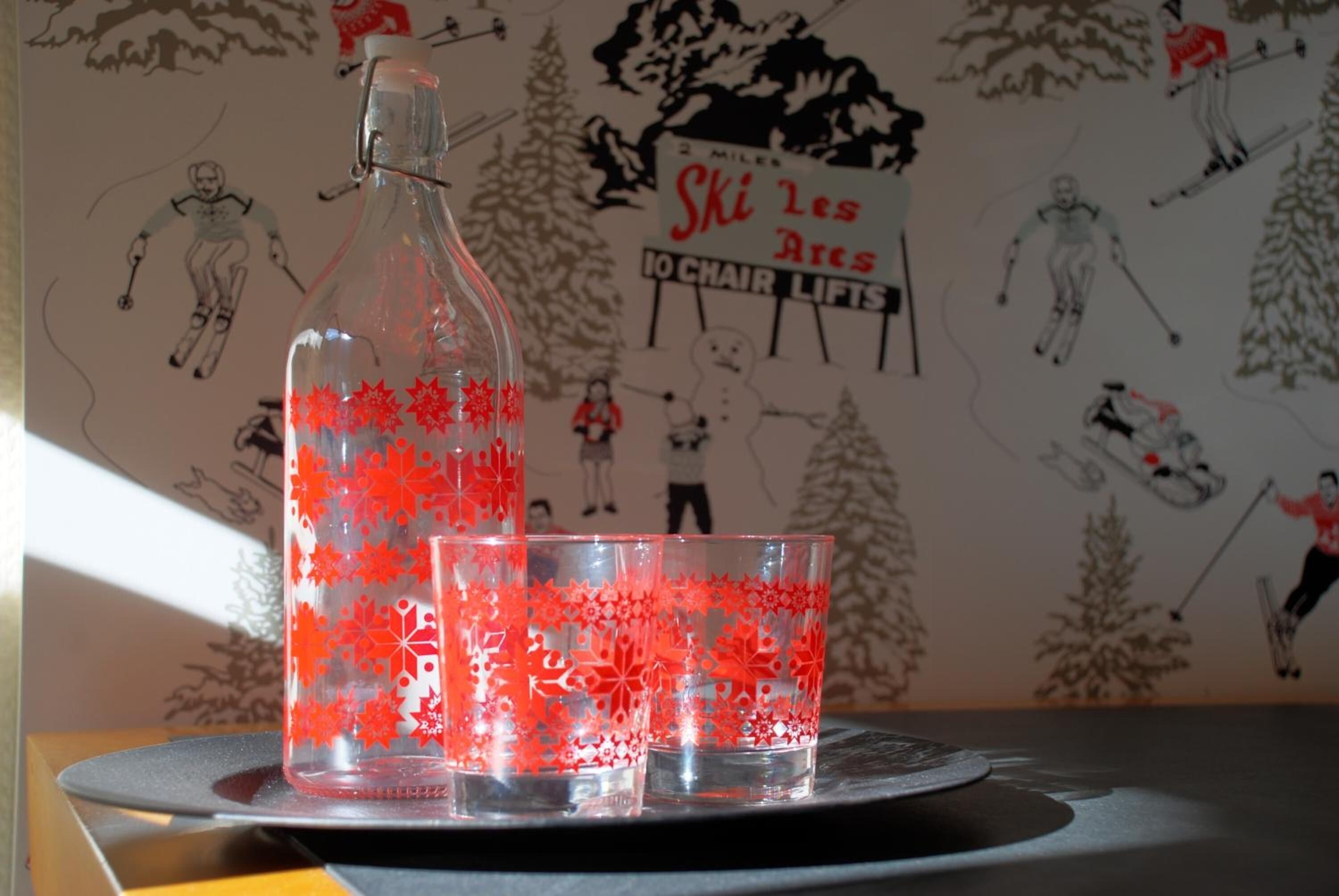 A bottle and two glasses with red snowflake designs on a coaster.