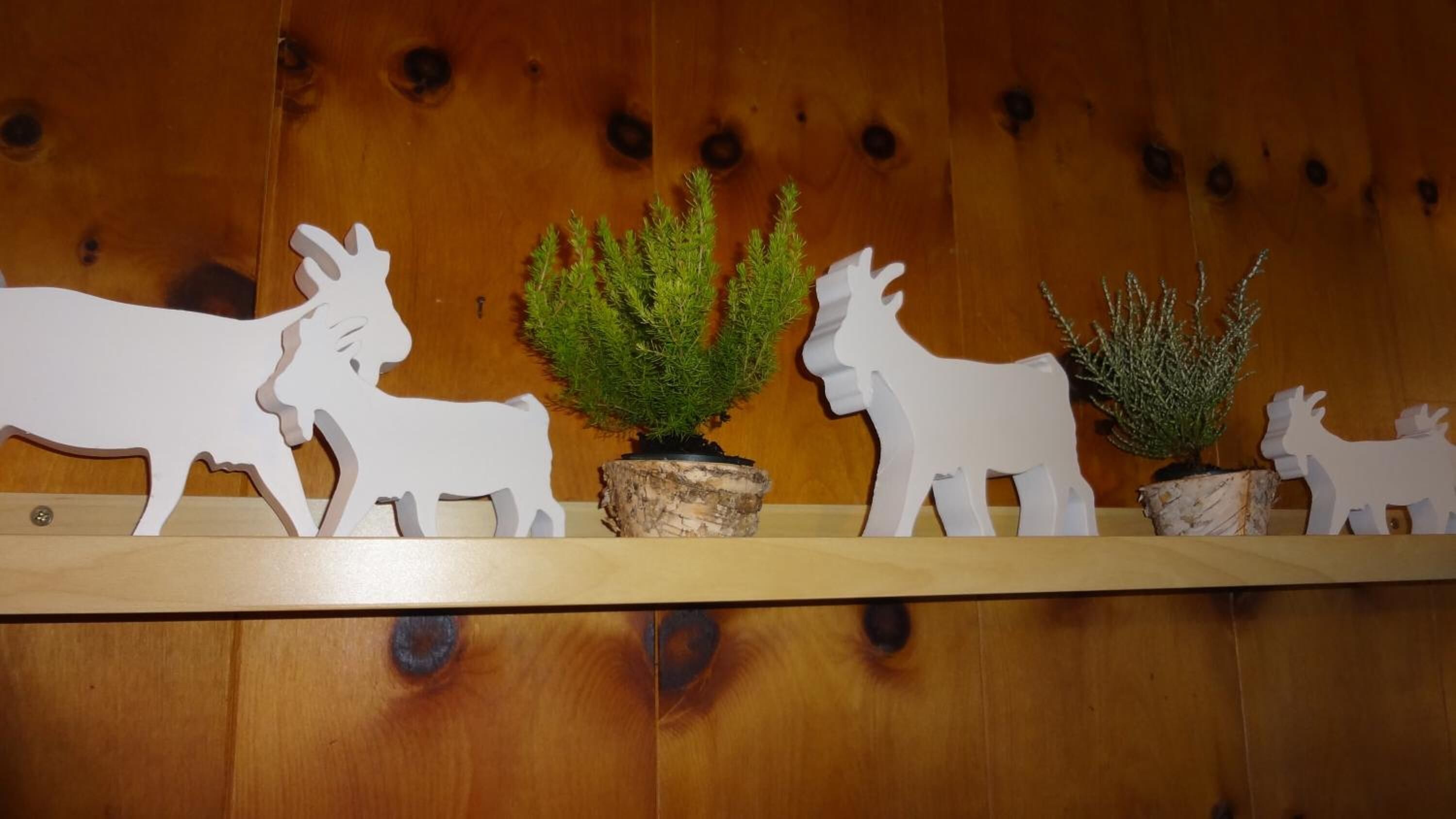 A wooden shelf with white paper cutouts of animals and small potted plants.