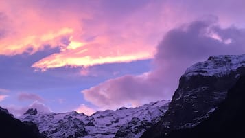 Paisagem montanhosa com picos cobertos de neve e céu com nuvens rosa e roxas.