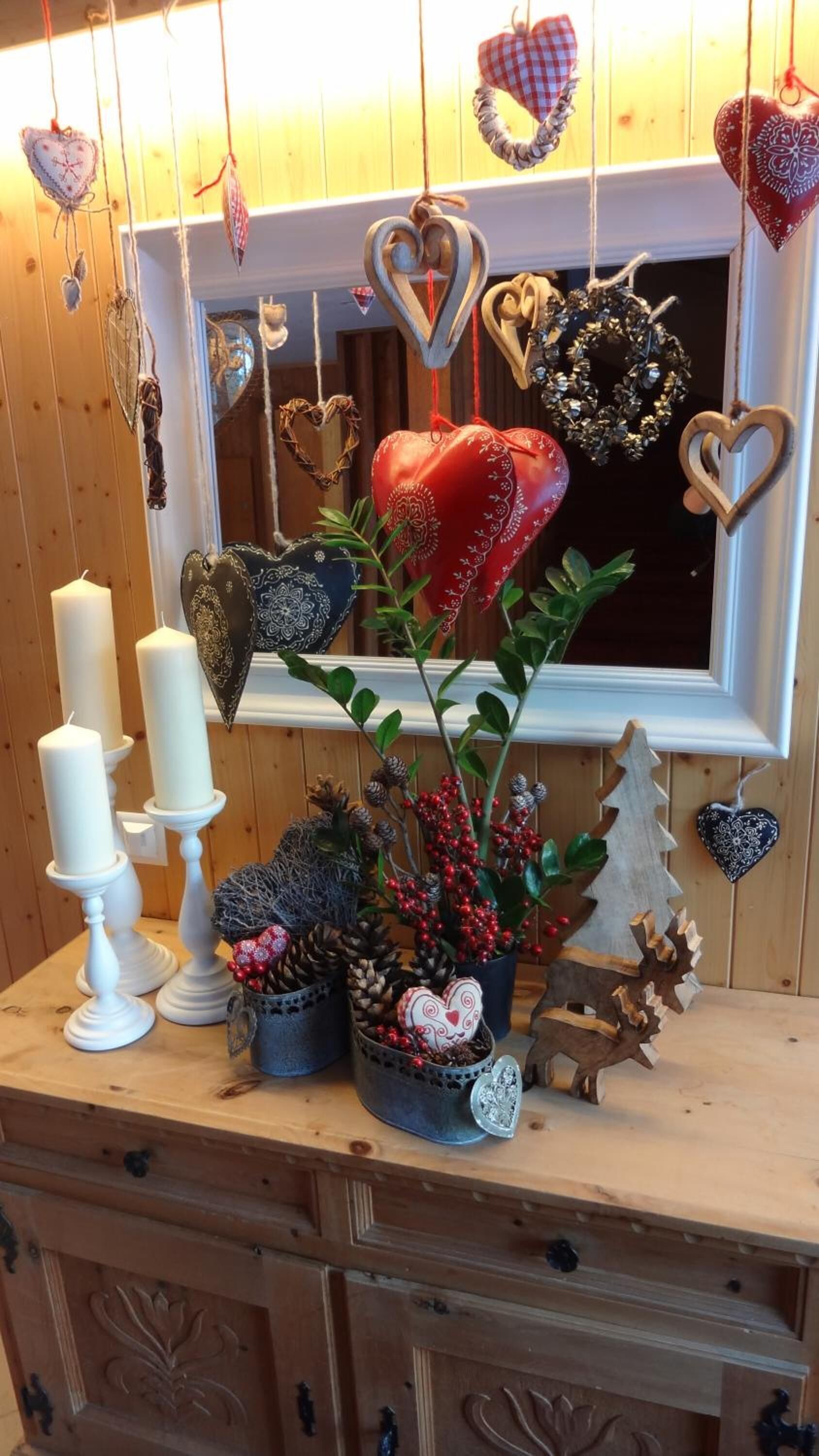 A wooden cabinet with decorative items including candles, a potted plant with red berries, and heart-shaped ornaments.