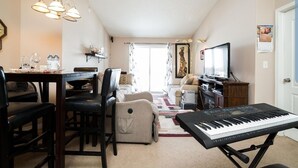 A cozy living room with a dining area, a piano, and a television. - 1 Clean & Cozy Private Bedroom with 1 Private Full Bath (Edmonton)