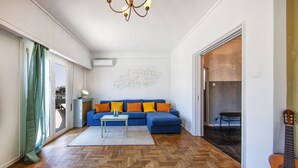 A living room with a blue sofa, a small table, a herringbone wood floor, and a guitar leaning against the wall. - Amazing Loft In Athens City Center (Athens)