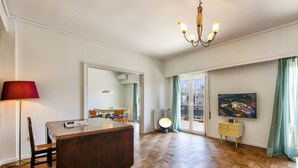 A spacious living room with a wooden floor, a dining area with chairs, a red lamp, a TV on a stand, and a large window with curtains. - Amazing Loft In Athens City Center (Athens)