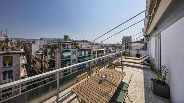 A rooftop terrace with a wooden table and chairs, potted plants, and a view of the cityscape. - Amazing Loft In Athens City Center (Athens)