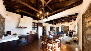 A rustic kitchen with wooden beams, a stone fireplace, and a dining area with a wooden table and chairs. - Beautiful Tranquil Stone Cottage (Zagora-Mouresi)