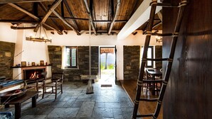 A rustic interior with a stone fireplace, wooden beams, and a stone wall. - Beautiful Tranquil Stone Cottage (Zagora-Mouresi)