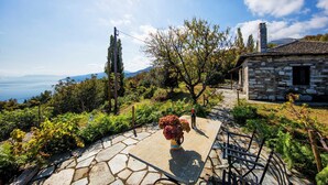 A stone house with a stone pathway leading to a table with a vase of flowers. - Beautiful Tranquil Stone Cottage (Zagora-Mouresi)