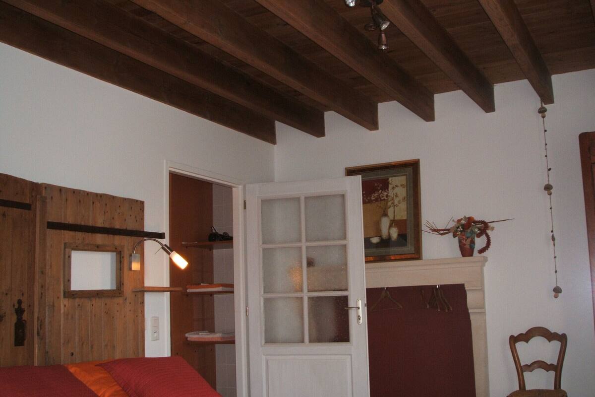 A room with a bed, a wooden ceiling, a white door, and a painting on the wall.