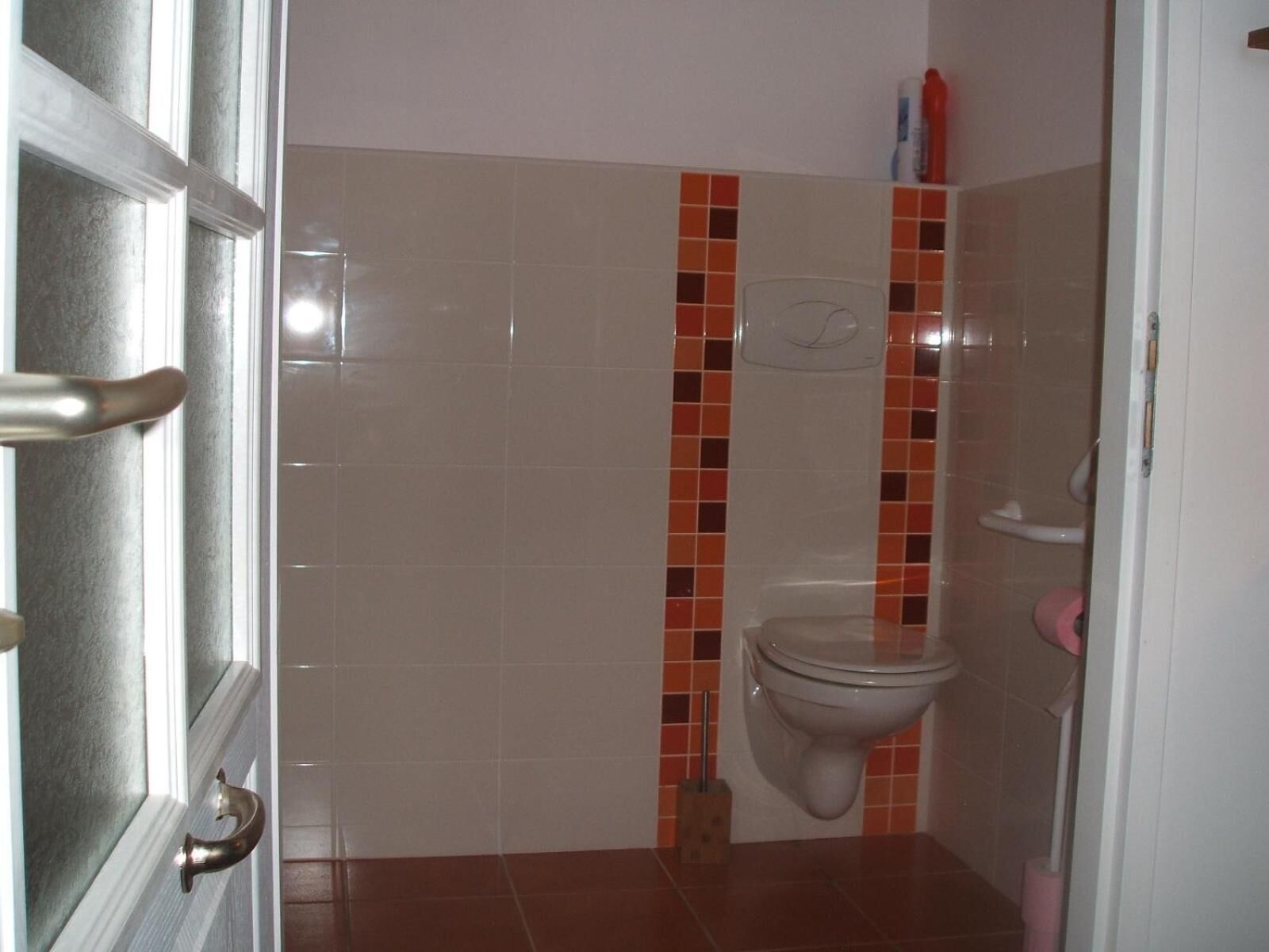 A bathroom with a toilet, a hand dryer, and a small shelf with toiletries.