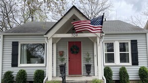 Una casa con puerta roja, porche delantero y una bandera estadounidense.