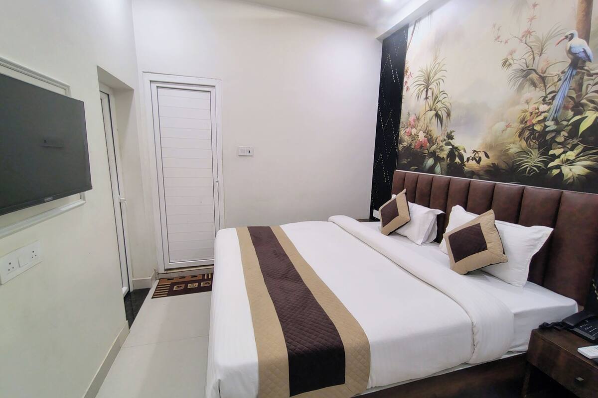 Une chambre d’hôtel avec un grand lit, un téléviseur fixé au mur, une porte et une fresque murale.