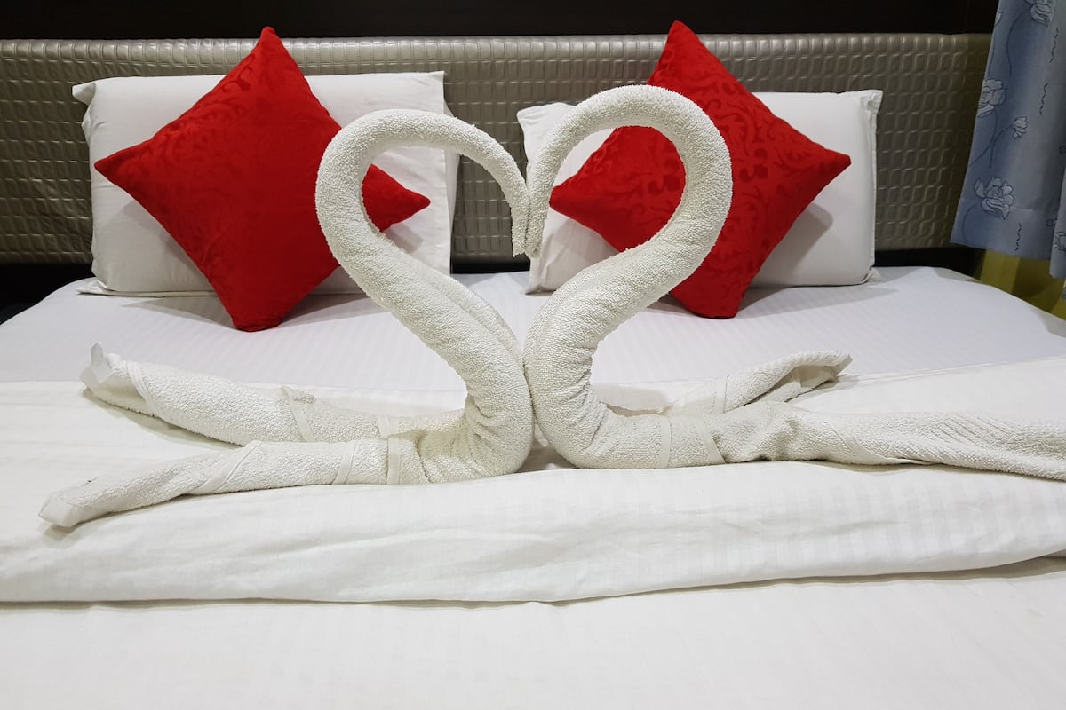 Un lit bien fait, avec du linge de lit blanc et des oreillers rouges, disposés en forme de cœur avec des serviettes.