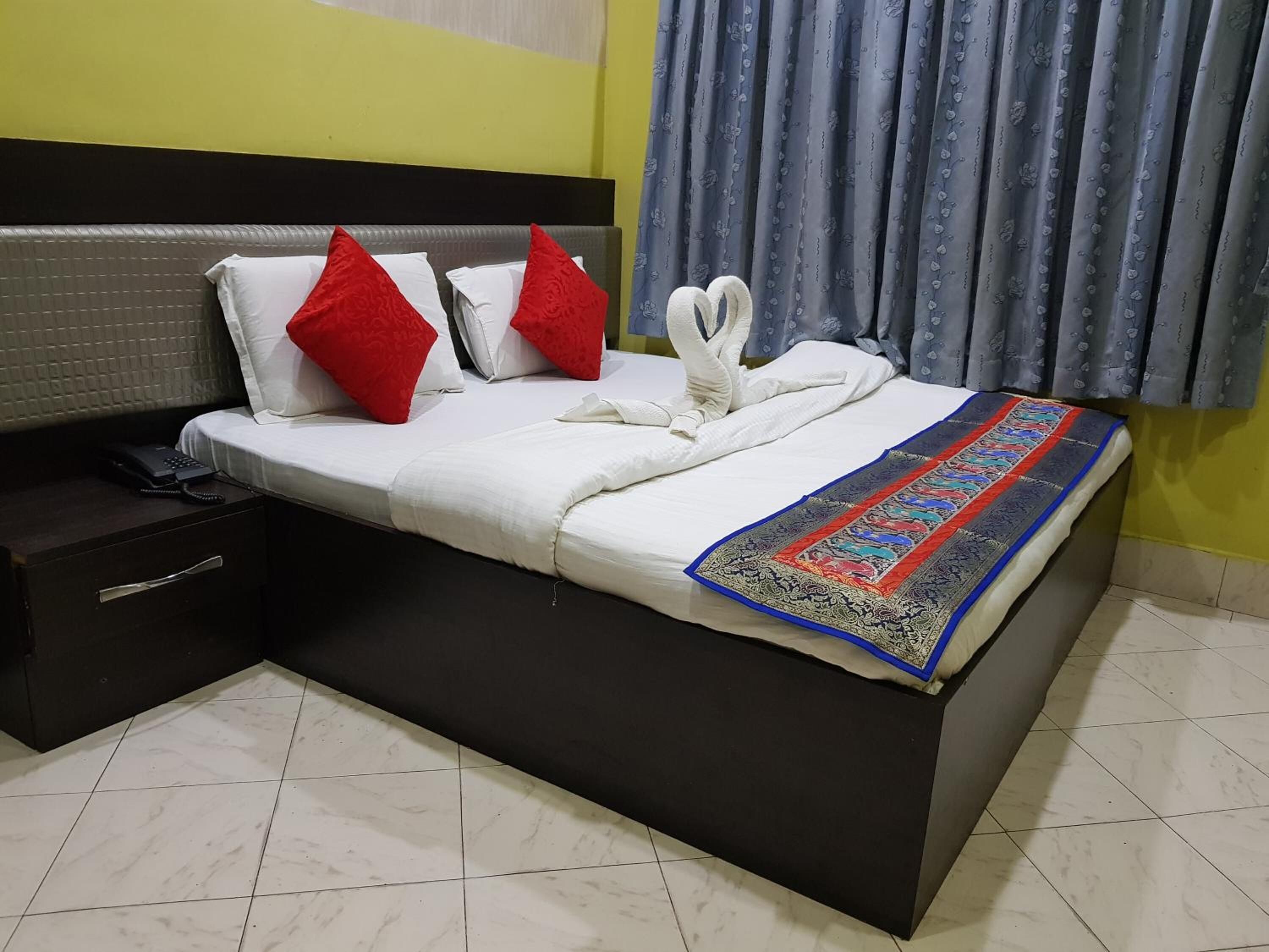 A neatly made bed with white bedding, red pillows, and a decorative blanket.