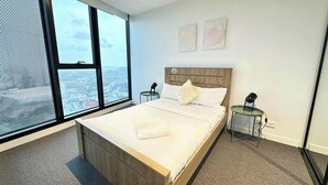 Een moderne hotelkamer met een groot bed, uitzicht op de stad en een klein nachtkastje met een lamp.