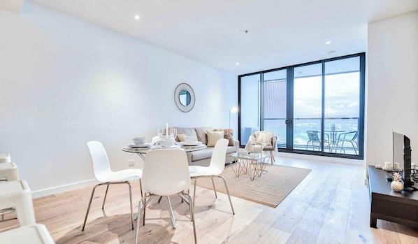A modern living room with a dining area, large windows, and a view of the city.