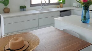 Een moderne keuken met witte kastjes, een groot raam en een eethoek met een houten tafel en een hoed.