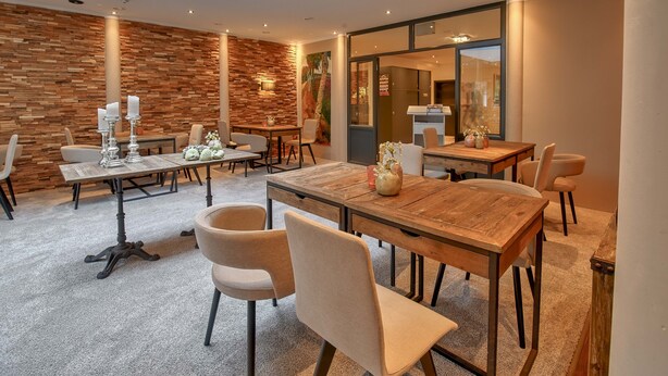 A modern dining area with wooden tables and chairs, a stone wall, and a large window. - Hotel Worpsweder Tor (Worpswede)