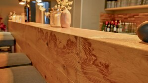A wooden bar counter with a vase of flowers and bottles in the background. - Hotel Worpsweder Tor (Worpswede)