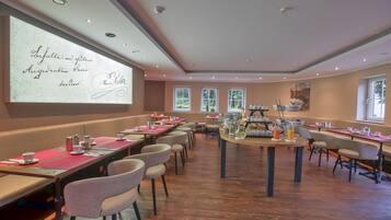 Un salón de conferencias con una amplia pantalla de proyección mostrando texto, mesas de madera con sillas y una estación de café.