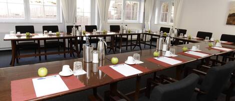 A conference room with long tables, chairs, and various amenities like water bottles, apples, and coffee pots.
