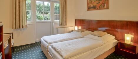 A hotel room with two beds, a wooden headboard, a painting on the wall, and a window with curtains.