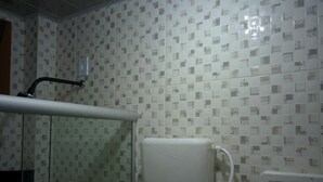 A bathroom with a tiled wall, a toilet, a shower area, and a glass partition. - Hotel e restaurante Toraryca (Belém)
