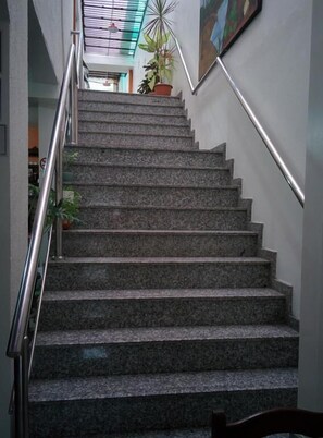 Un escalier avec des marches en granit, une rampe métallique et un pot de fleurs au sommet.
