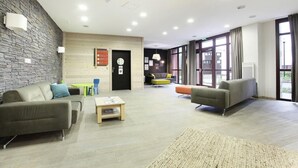 A modern lobby with a stone wall, a reception desk, a seating area with sofas, and large windows. - Wifi, 100m from resort center, swimming pool, balcony, tv, ski locker, 58m², Flaine (Flaine)