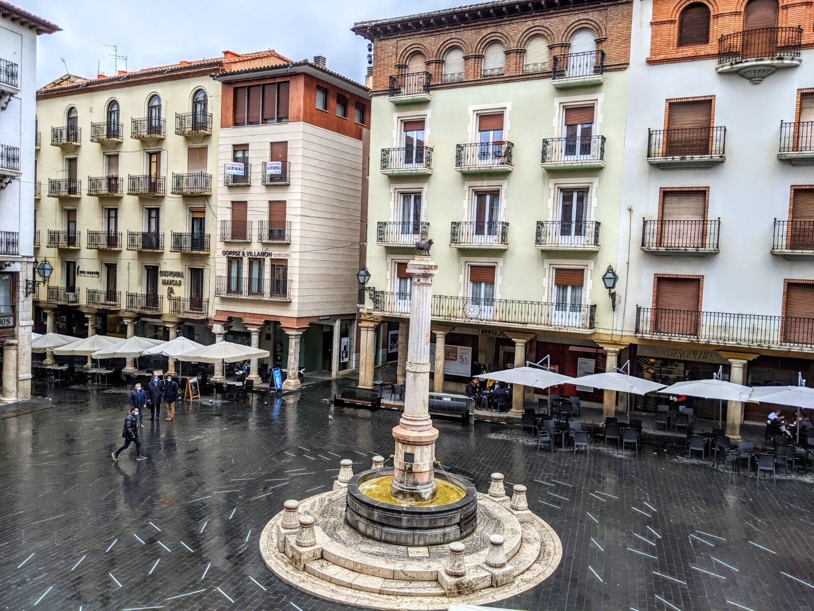 A plaza with a central fountain, surrounded by buildings with balconies and outdoor seating.