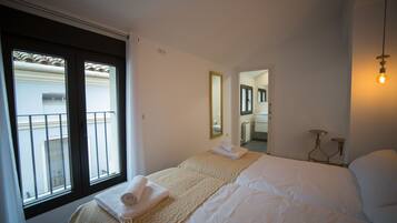 A bedroom with a bed, a window, a mirror, and a bathroom visible through an open door.