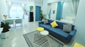 Ein modernes Wohnzimmer mit einem blauen Sofa, gelb-weißen Beistelltischen, einem großen Spiegel und einem Essbereich mit einem weißen Tisch und Stühlen.