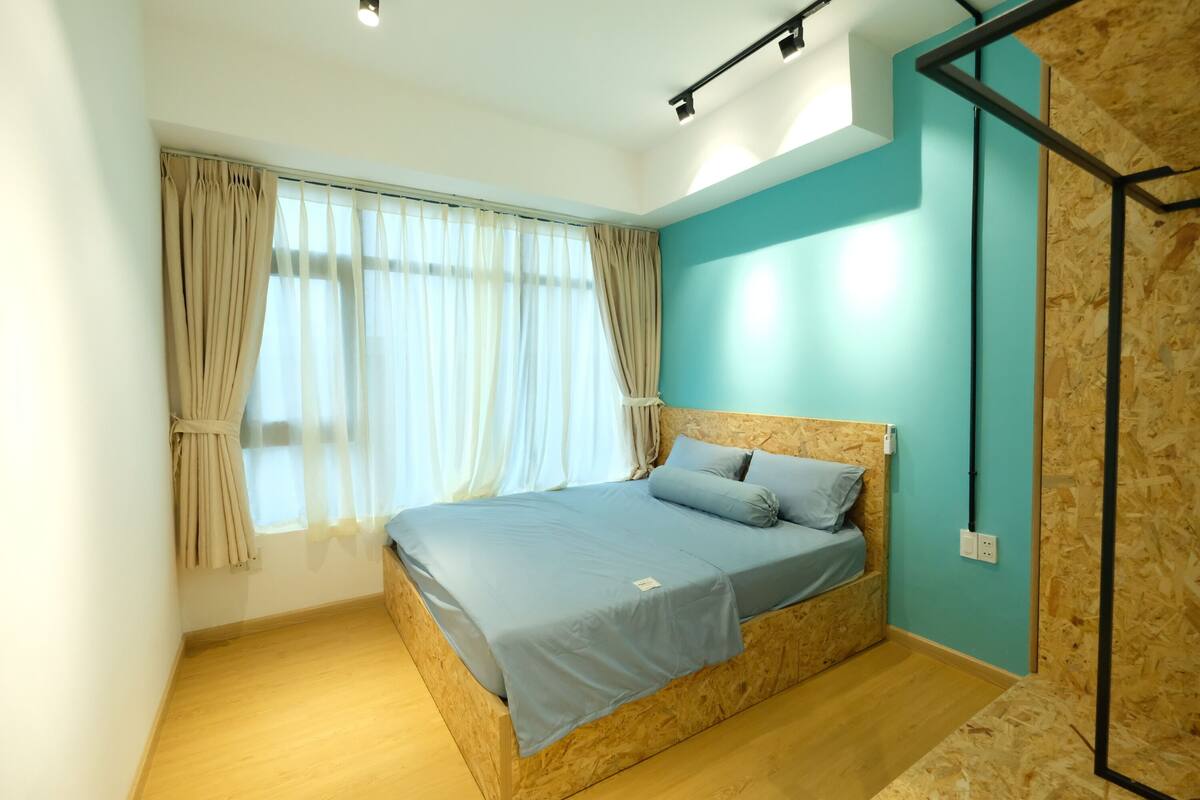 Ein Schlafzimmer mit einem hölzernen Bett, einer Wand in Türkis und einem großen Fenster mit Vorhängen.
