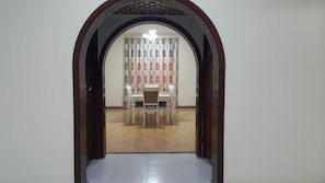 An arched doorway leading to a dining area with a table and chairs, a patterned curtain, and a chandelier.