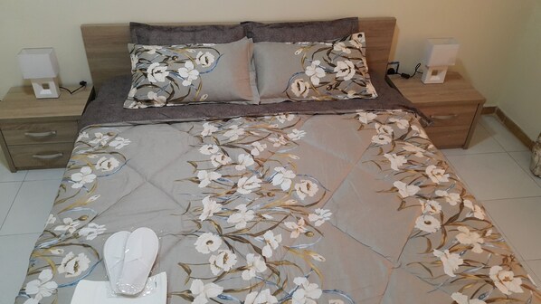 A neatly made bed with floral bedding, two pillows, and a bedside table with a lamp and a speaker.