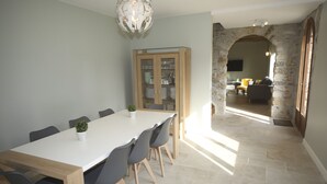 A dining area with a long table, chairs, a cabinet with glass doors, and a stone archway leading to another room. - Beautiful house to share with friends or family (Nanteuil-sur-Marne)