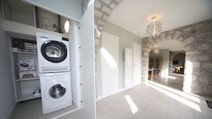 A laundry room with a front-loading washing machine and a dryer, a stone wall, and a chandelier. - Beautiful house to share with friends or family (Nanteuil-sur-Marne)