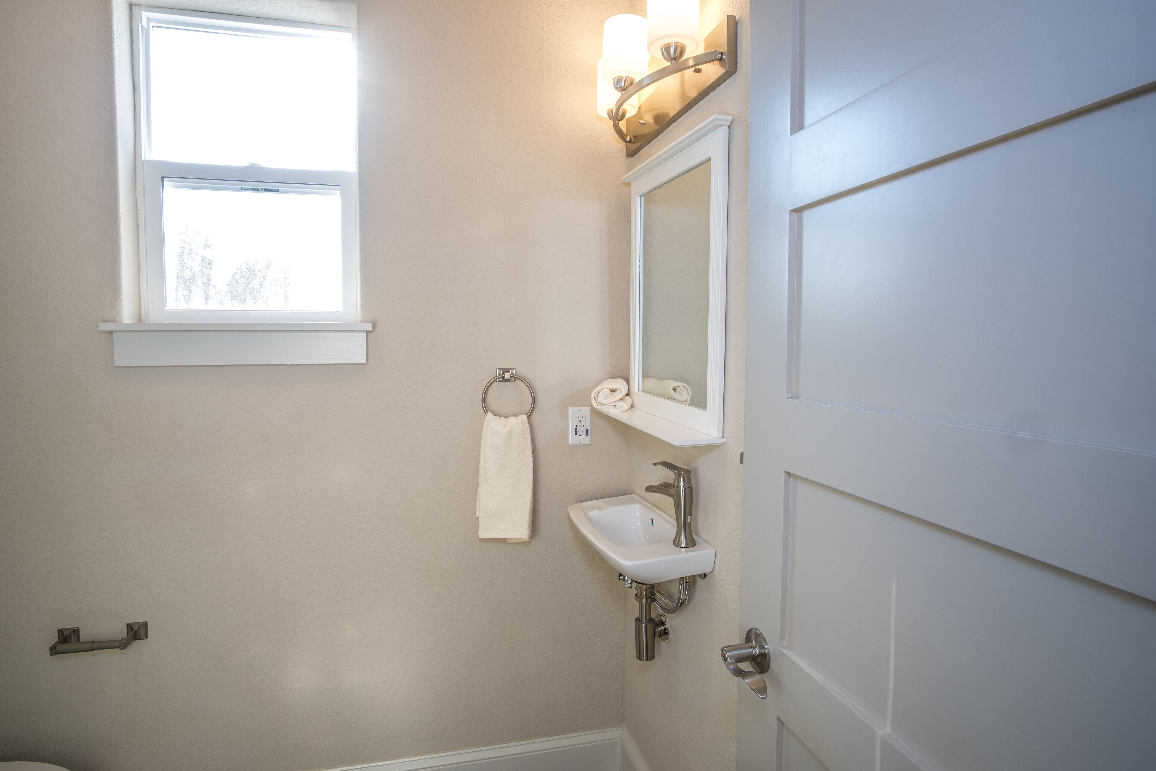 A bathroom with a window, a sink, a mirror, and a towel rack.