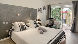 A bedroom with a bed, a nightstand, a lamp, and a view of an outdoor patio with a table and chairs. - Mas Maurane Chambre d'hôtes (Tarascon)