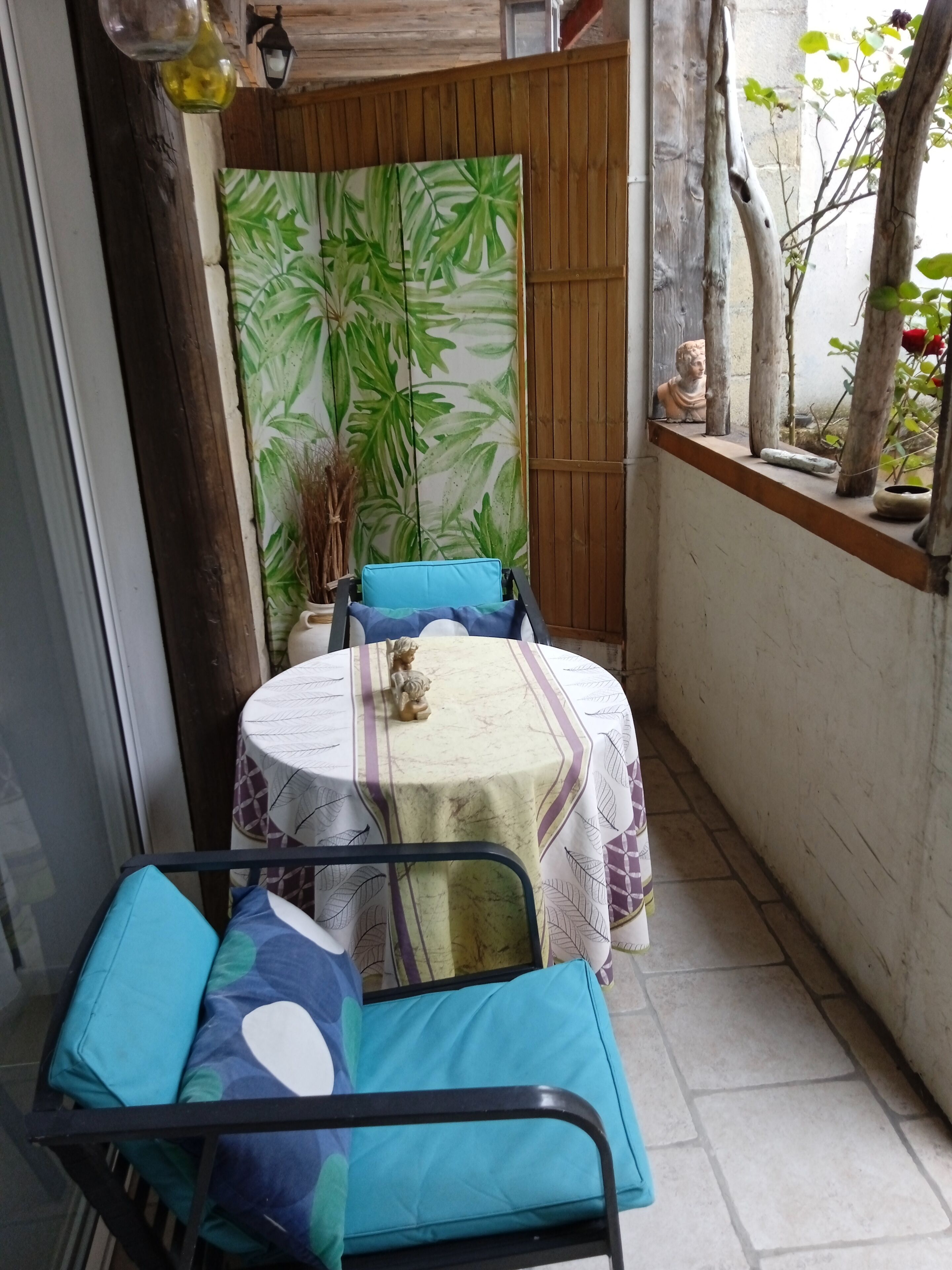 A small patio area with a round table covered by a white tablecloth and a blue cushion. A potted plant is visible in the background.