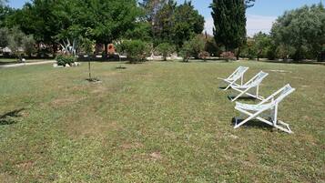 Een gazon met drie witte lounge fauteuils en een kleine boom.