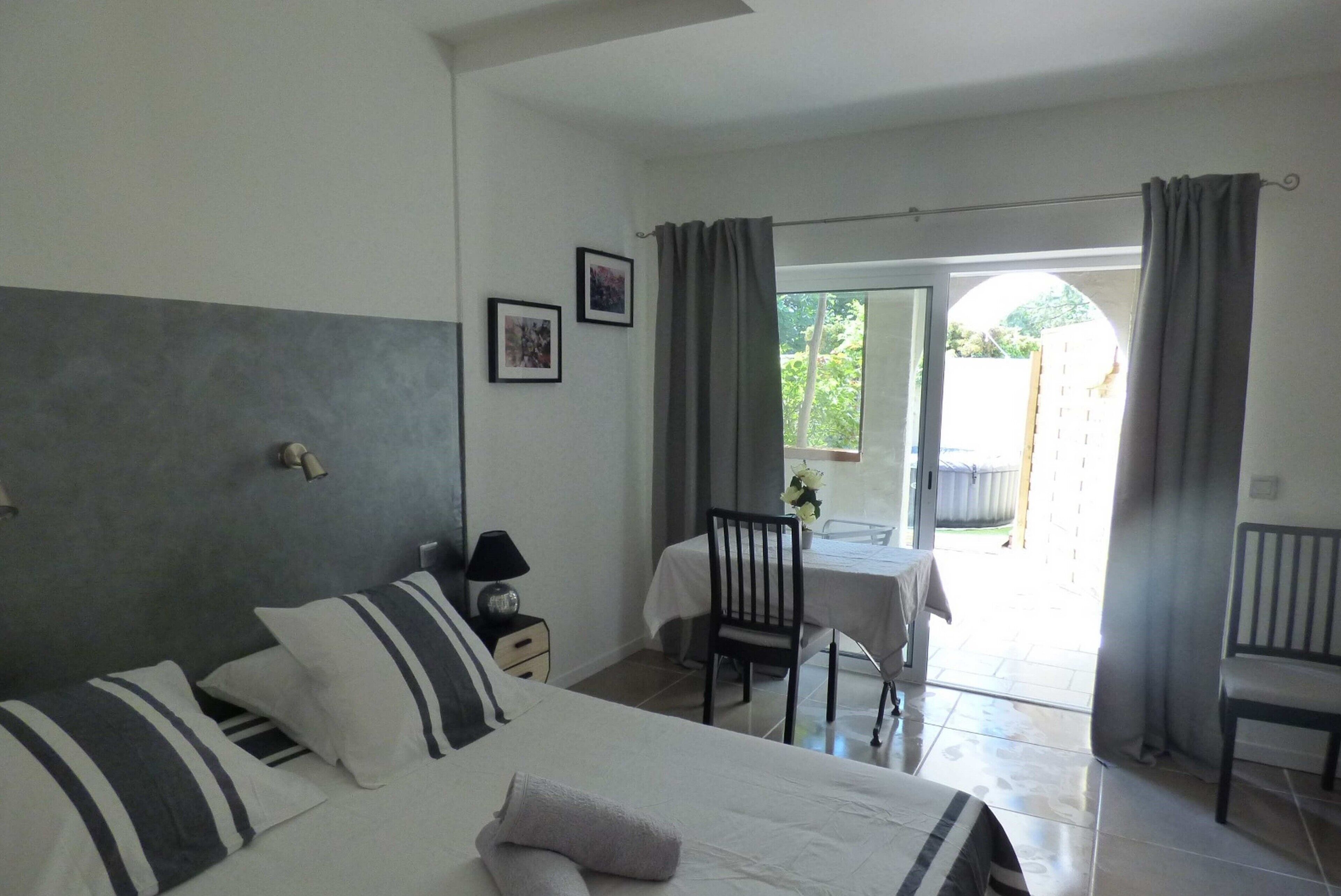 A hotel room with a bed, a desk, and a chair. There is a window with curtains and a view of the outside.